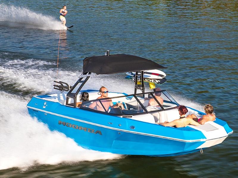 Five people riding a blue Moomba Helix as it tows a wake-boarder through the water.