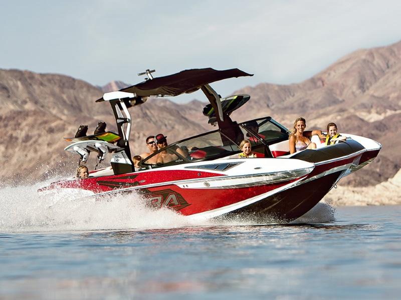 Red Supra SE wakeboard boat full of passengers cruising through the water.